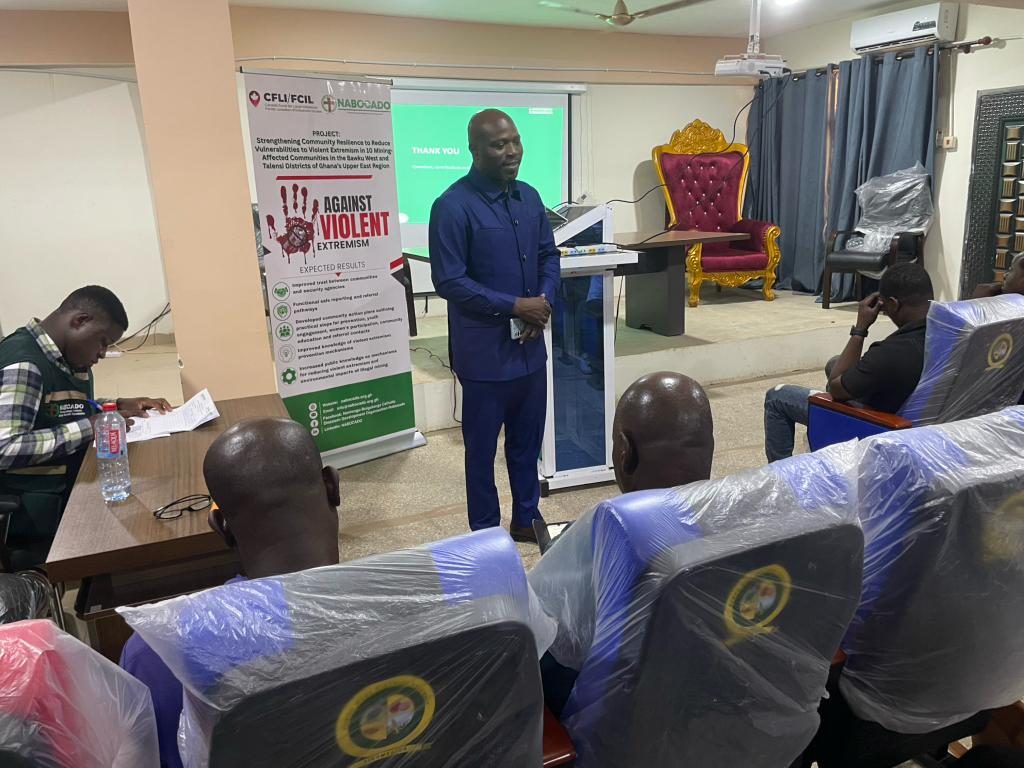 A speaker addresses participants beside the project’s “Against Violent Extremism” banner